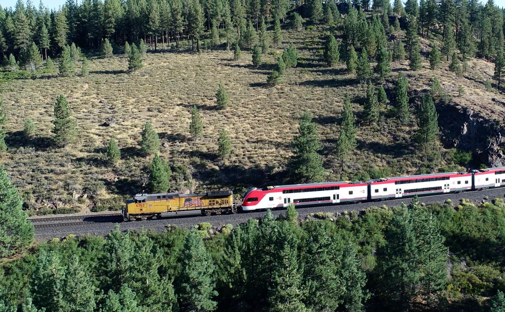 Caltrain electric trainsets being pulled by a locomotive through a scenic forest
