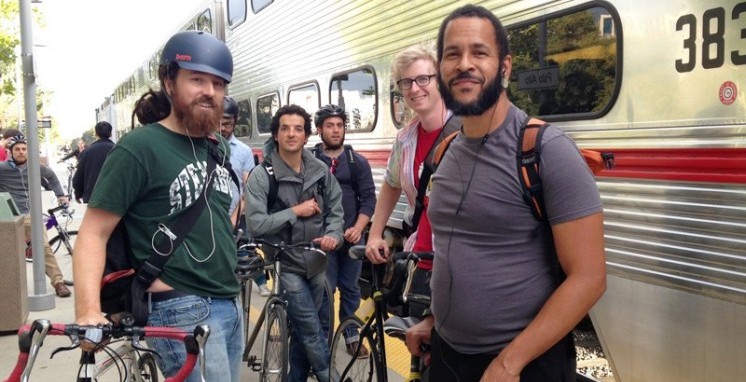Many bikers congregate outside on a Caltrain platform. Bikers as in people with bicycles, not the Sons of Anarchy kind of bikers. 