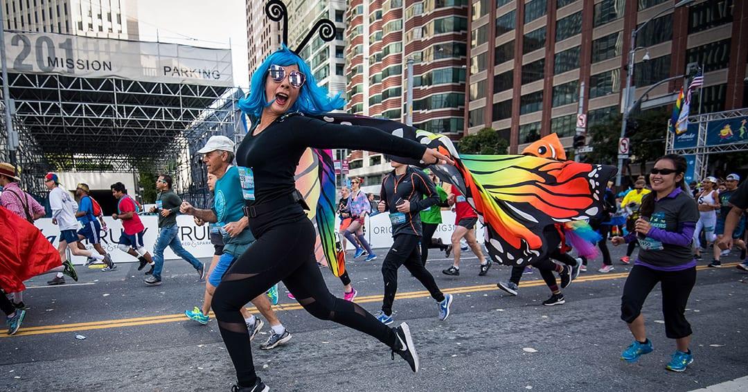 A Bay to Breakers attendee in a blue wig and a fabulous butterfly costume runs gleefully