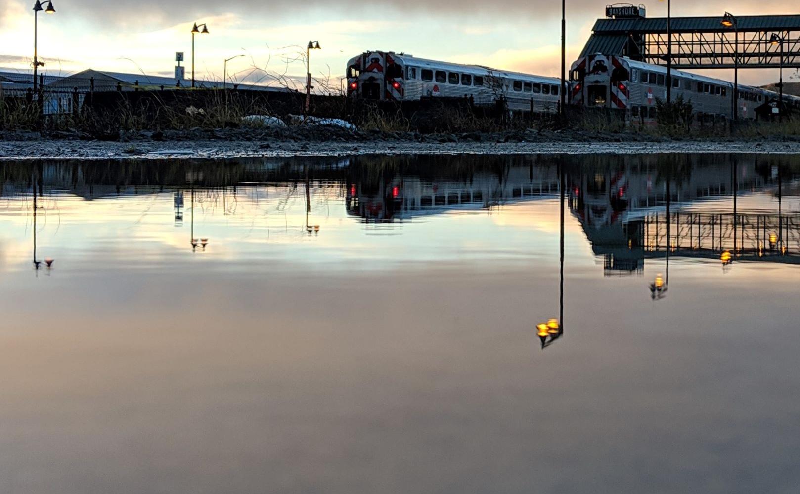 Spectacular photo of a southbound train pulling through the Bayshore station, also reflected in the water in the foreground